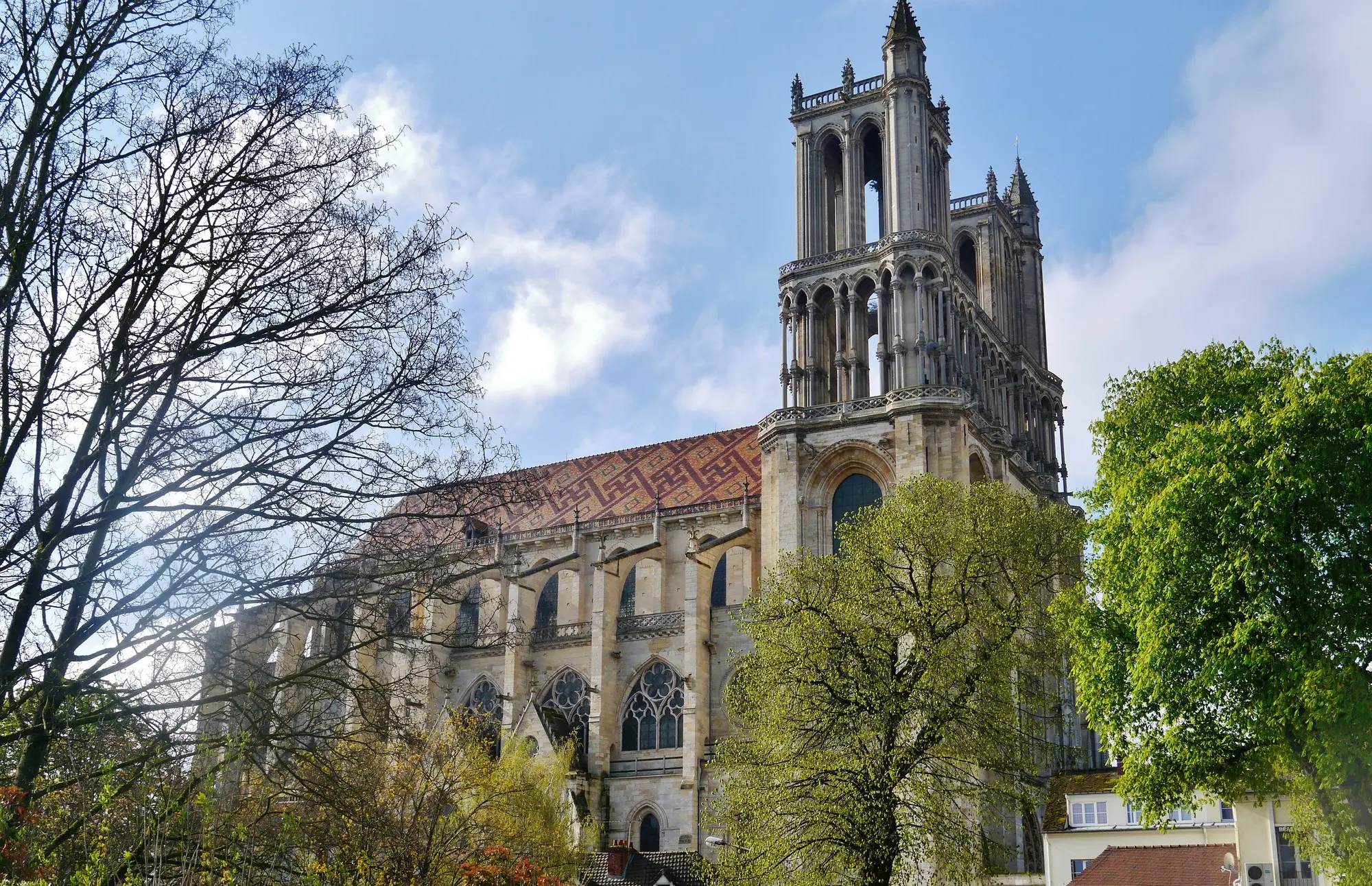 La collégiale Notre-Dame de Mantes-la-Jolie, sa tour et son toit de tuiles vernissées, entre les arbres au printemps