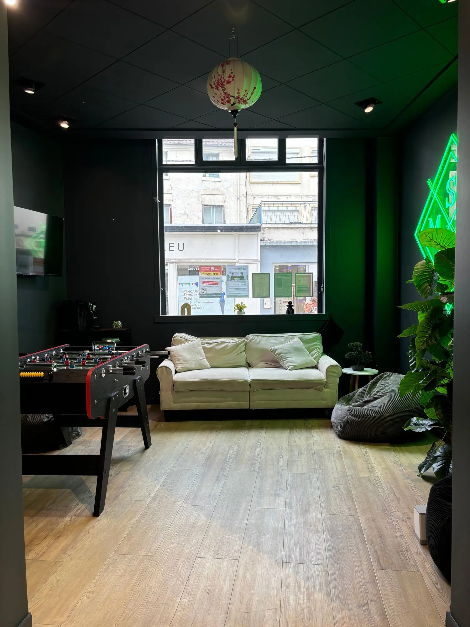 Espace détente : babyfoot, canapé, néon vert et grande baie vitrée sur la rue