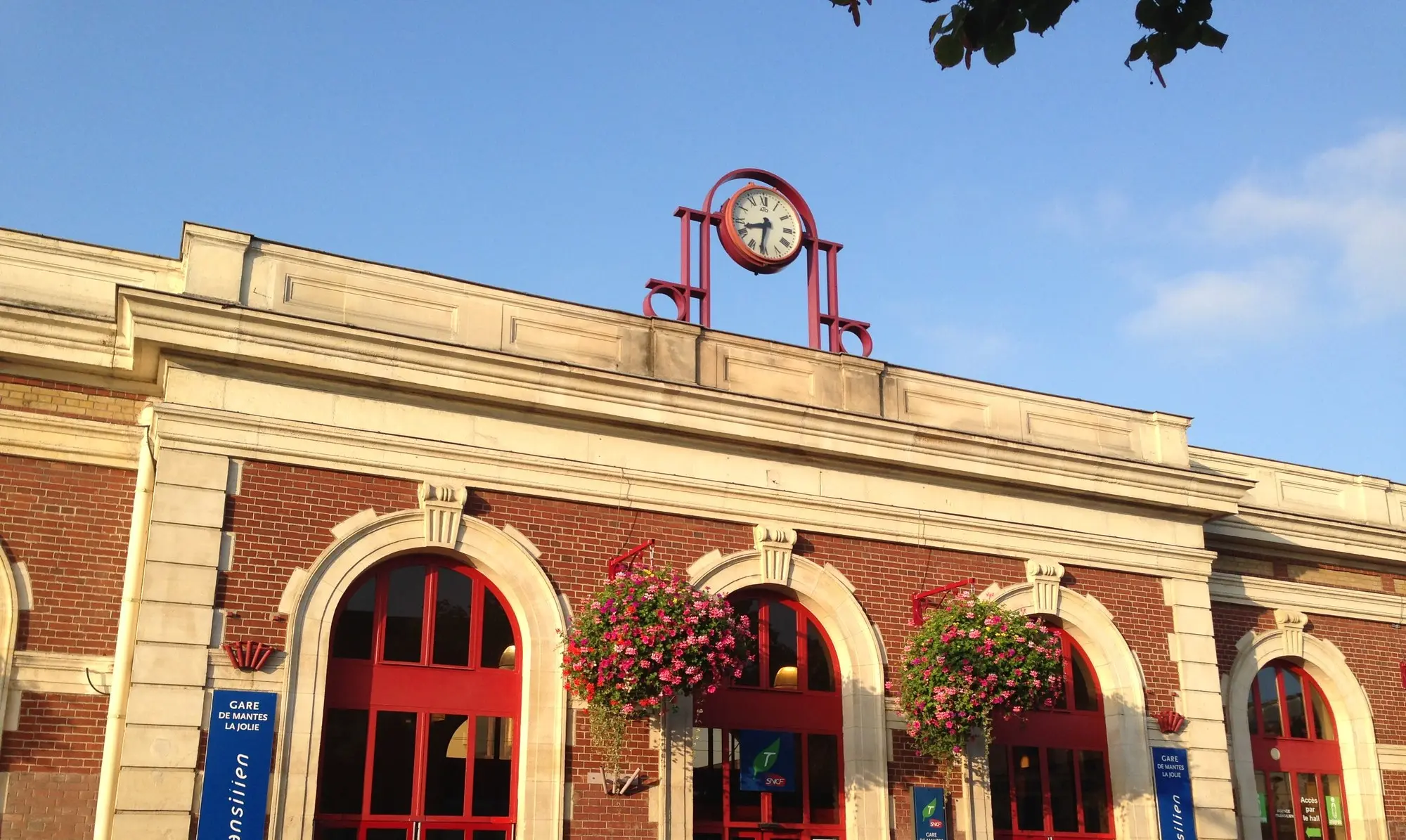 La façade de la gare de Mantes-la-Jolie, en brique et pierre, avec son horloge et ses suspensions fleuries