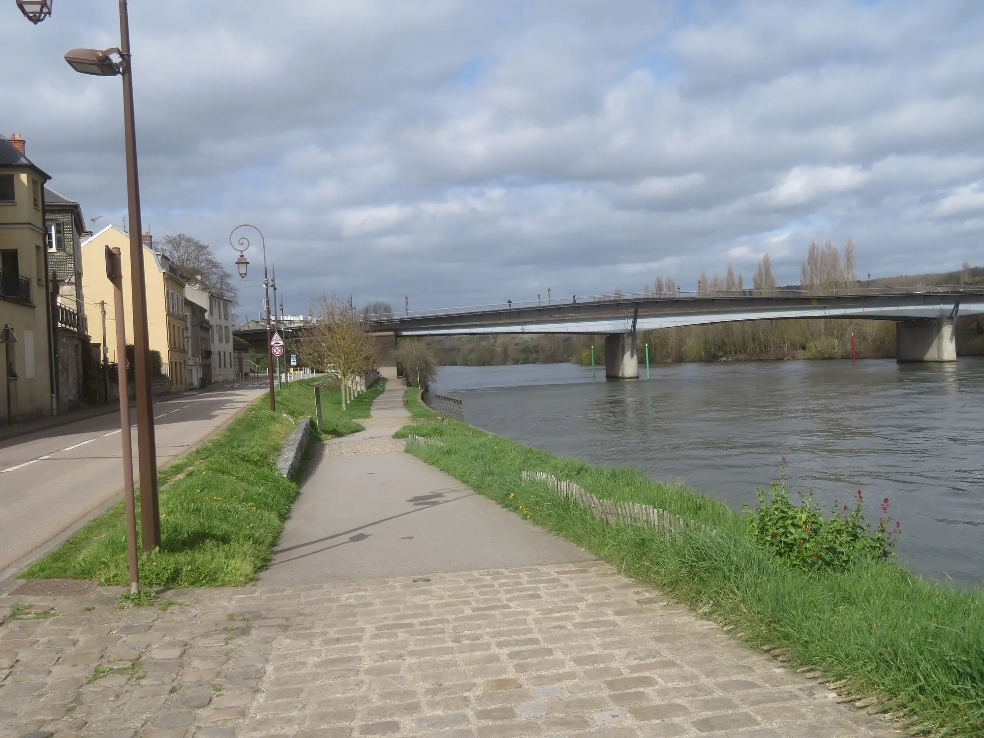 Le quai des Cordeliers au bord de la Seine, une promenade pavée et herbue, et un pont au loin
