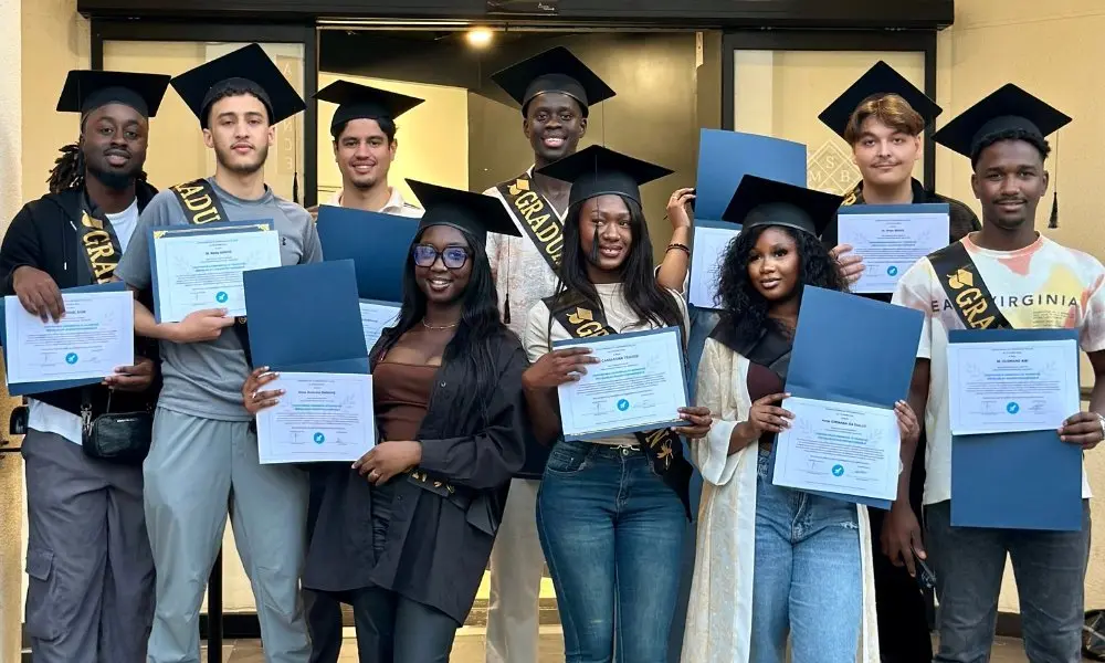 Huit diplômés en toge et chapeau de diplômé, leur diplôme à la main, lors de la cérémonie de remise